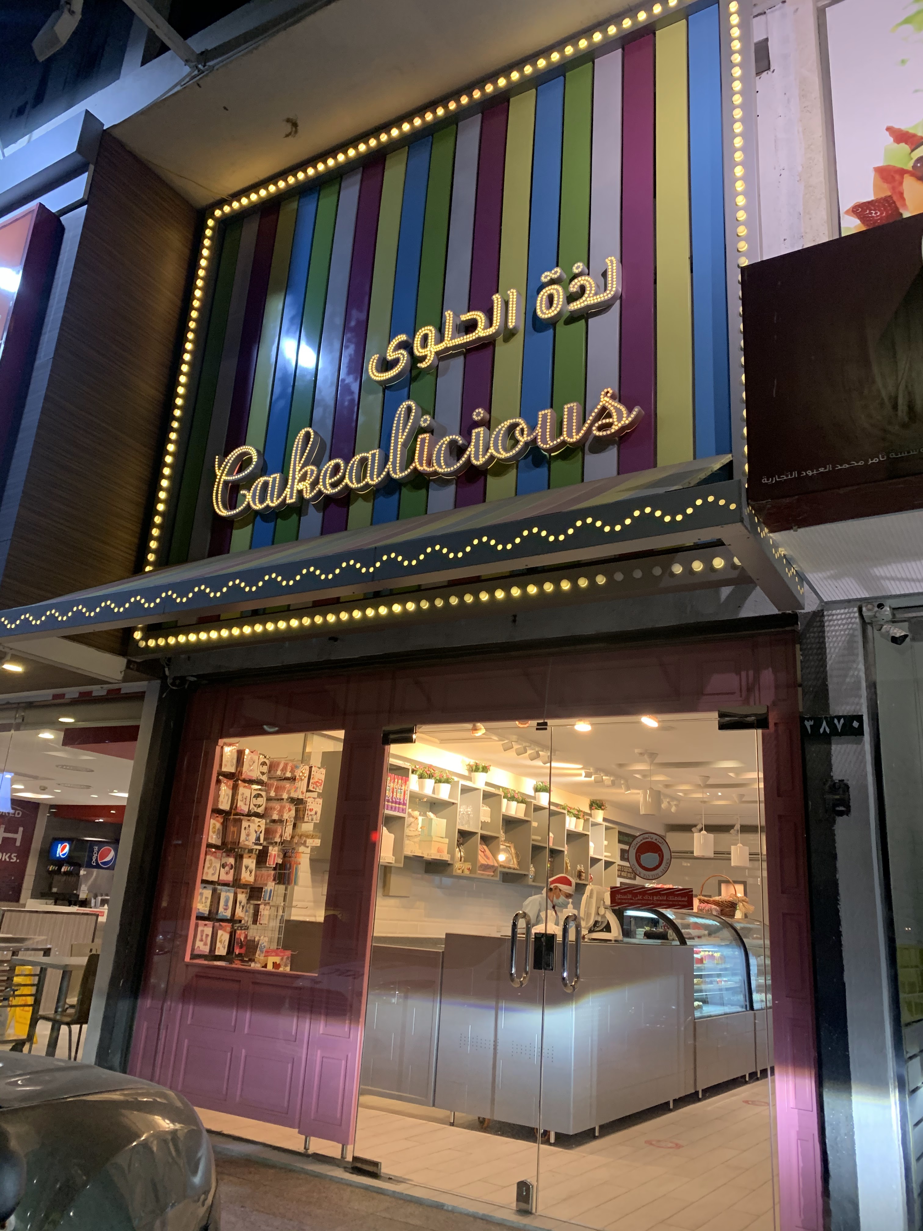 واجهة لذة الحلوى بخطوط عمودية بألوان قوس قزح ولمبات ذهبية حول لوحة المحل